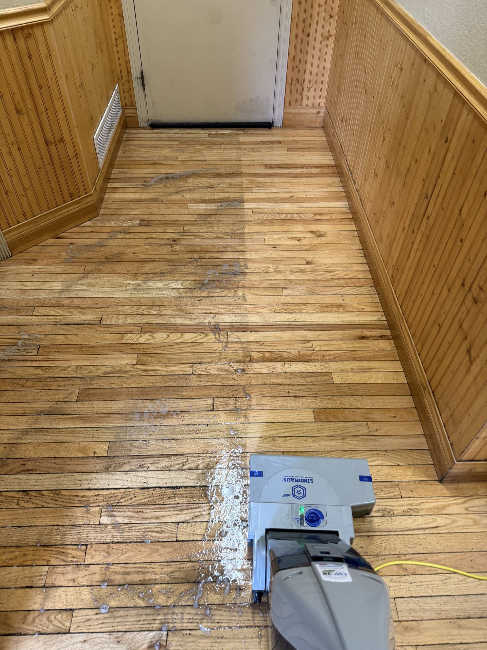 Professional hardwood floor cleaning in progress using a Lindhaus machine, showing a clear before-and-after difference on a dirty, worn wood floor in a Summit County Colorado home hallway. Professional hardwood floor cleaning service is performed by Exclusive Cleaning and Restoration
