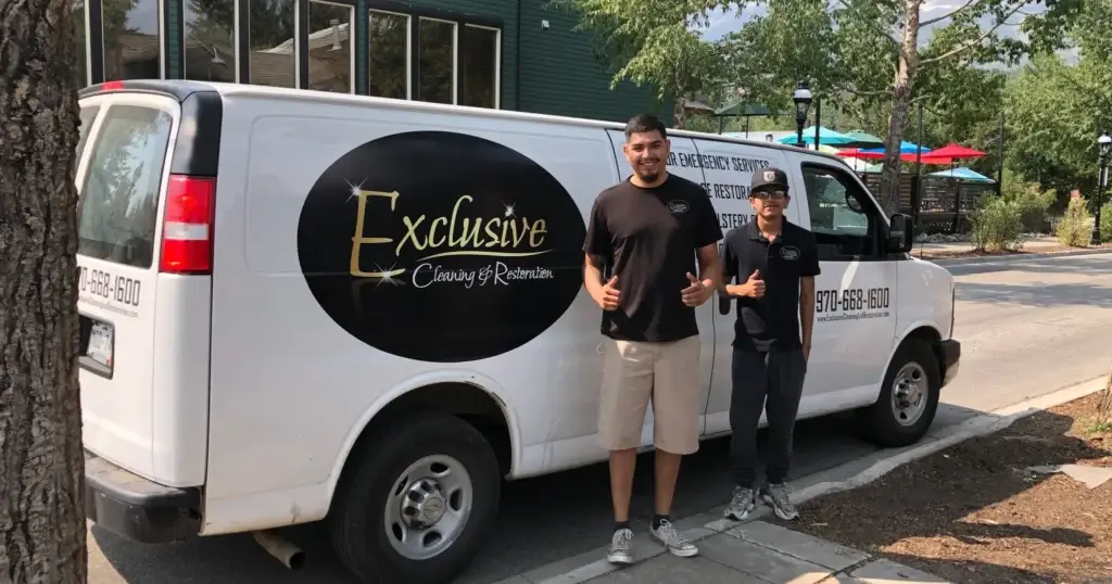 Two workers in uniforms stand next to a van with the logo Exclusive Cleaning and Restoration in Breckenridge, CO.