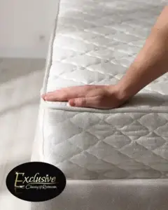 A hand on a bare mattress with the Exclusive Cleaning and Restoration logo in the corner